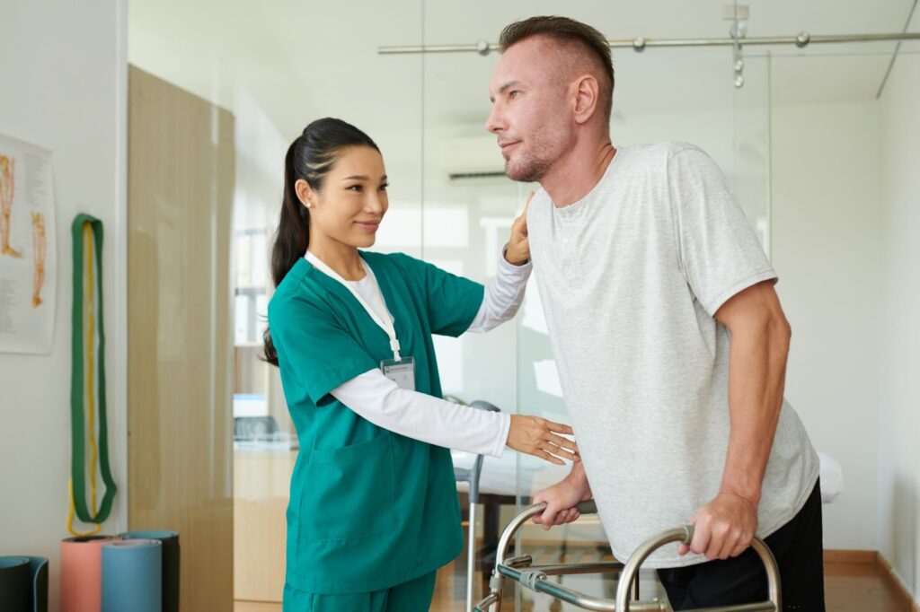 Nurse supports a man learning to walk with a walker.